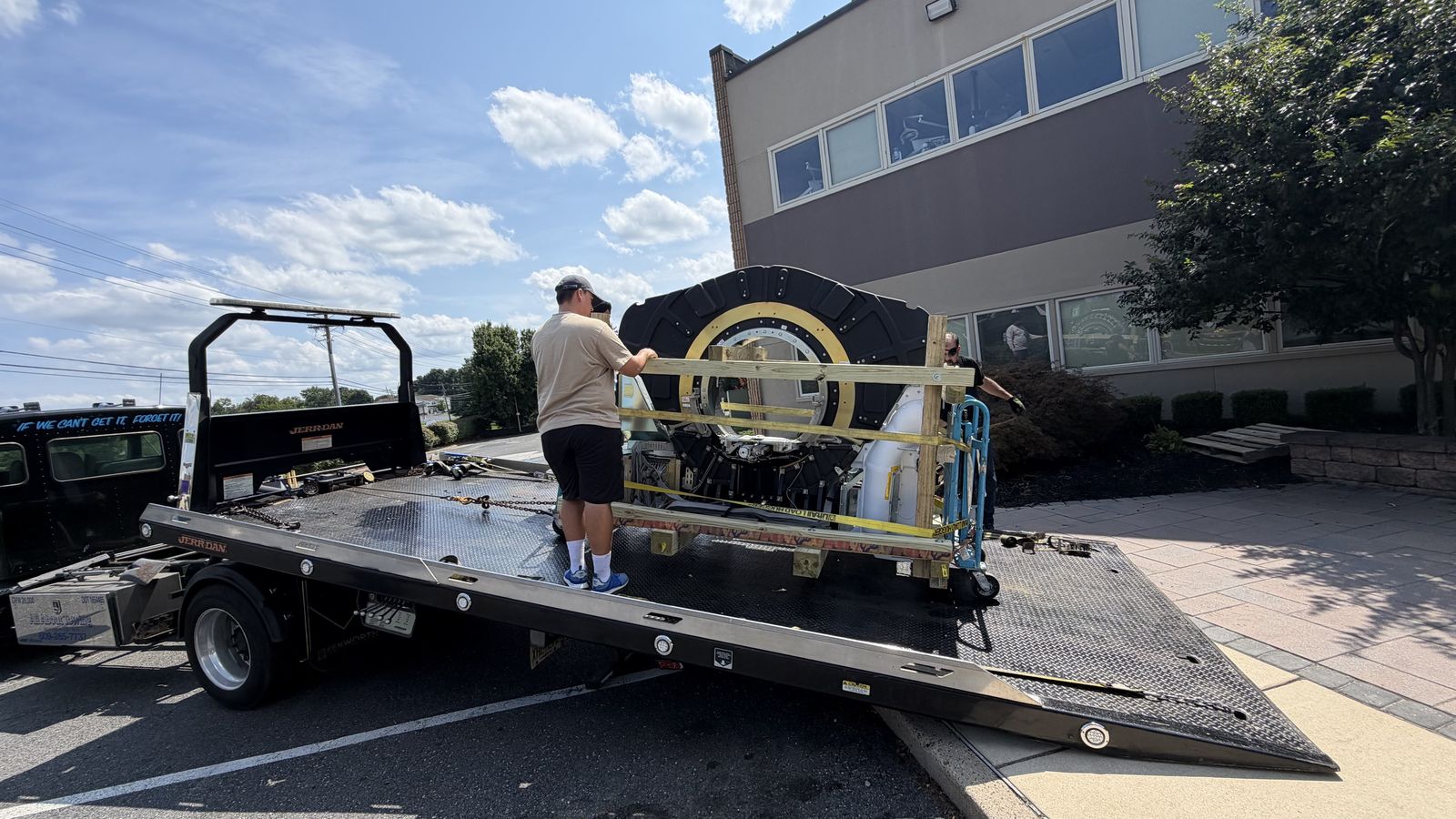 Crated PET/CT gantry on a flatbed tow truck deck being loaded by the crew