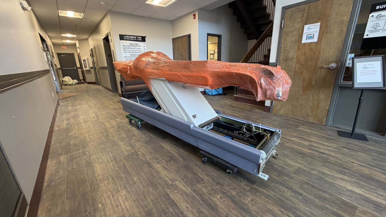 Wrapped PET/CT patient table on dollies rolling through the building hallway